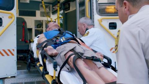 waxwork dummy strapped in a gurney being raiseed into an ambulance by two men