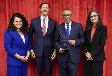 a group of three people standing with the award recipient, who is holding a commemorative trophy