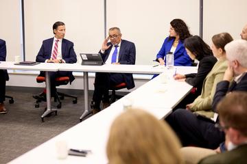 people sitting around a conference-style table setup with the award recipient, listening to him speak in a meeting/panel setting. 