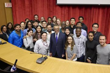 a large group of students and others gathered with the award winner in a classroom